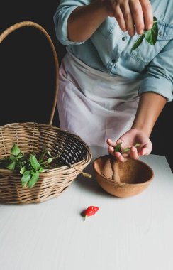 Tahta masa ve siyah arka planda taze otları kullanan bir kadın. 