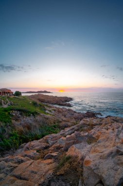 Jagged kıyı kayaları, Isola Rossa, Sardinya, İtalya. Renkli alacakaranlık gökyüzü. Deniz yüzeyinde gün batımı.