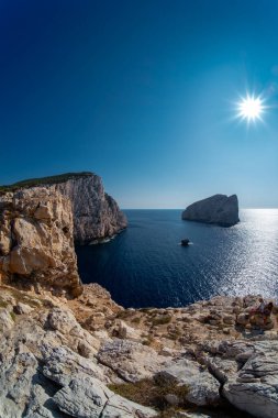 Capo Caccia 'da sakin deniz tarafından yıkanan kayalık kıyı oluşumunun resimli görüntüsü. Güneşe karşı görüş. Yaz güneşli gün manzarası açık gökyüzü.