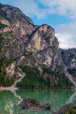 Güney Tyrol, İtalya 'daki Braies Gölü' nün berrak turkuaz suyunun üzerindeki muhteşem yüksek kaya duvarının manzarası. Sonbahar dağları manzarası.