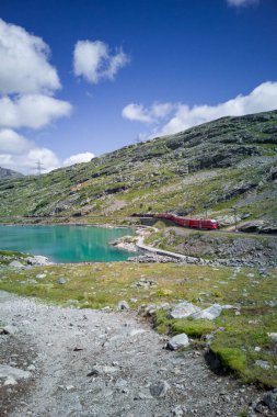 Kızıl Bernina Ekspres treni İsviçre Alpleri 'nde turkuaz gölden geçiyor. Panoramik antrenörlü ve genişletilmiş pencereli gezici tren.