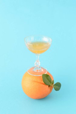 Portakal suyuyla dolu bir bardak, mavi arka planda yeşil yaprakları olan bir portakalın üzerinde duruyor. Yaratıcı bir fikirle ferahlatıcı bir narenciye içeceği..