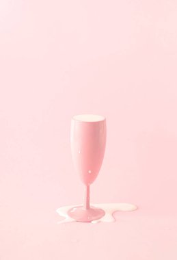Pembe şampanya bardağı ve dökülen süt. Pembe arkaplan.
