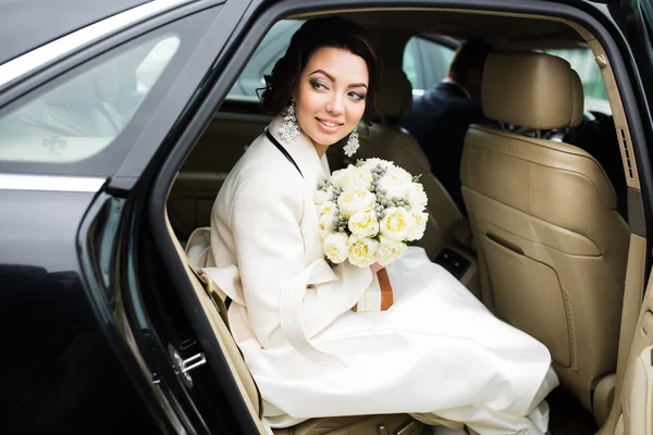 Trouwdag: mooie bruid met boeket van witte bloemen in de auto — Stockfoto