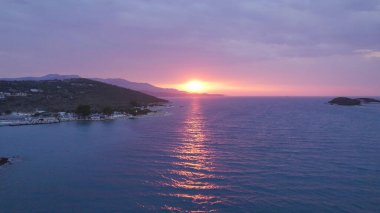 Drone view of Ksamil Albania showing the coastline at sunset with pink sun rays and purple skies over the sea