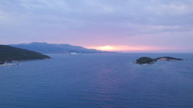Aerial view of Ksamil Albania at sunset showing the coastline, turquoise sea, and a cruise ship far on the horizon with colorful skies