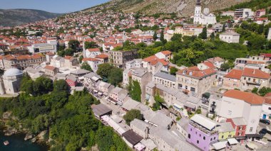 Mostar 'ın Neretva Nehri boyunca uzanan canlı renkli evlerini manzaralı tepeler ve Bosna-Hersek ikonik kentinin tarihi cazibesiyle gösteren insansız hava aracı fotoğrafı..