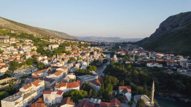 Mostar 'ın güzel şehir manzarasını gösteren hava aracı fotoğrafı Neretva Nehri ve Stari Most ikonik köprüsü, tarihi mimari ve manzaralı Balkan tepeleriyle çevrili..