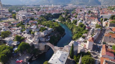Ünlü Stari Köprüsü 'nün altından akan Neretva Nehri' nin insansız hava görüntüsü çevresindeki tarihi binalar ve yeşil tepelerle çevrili..
