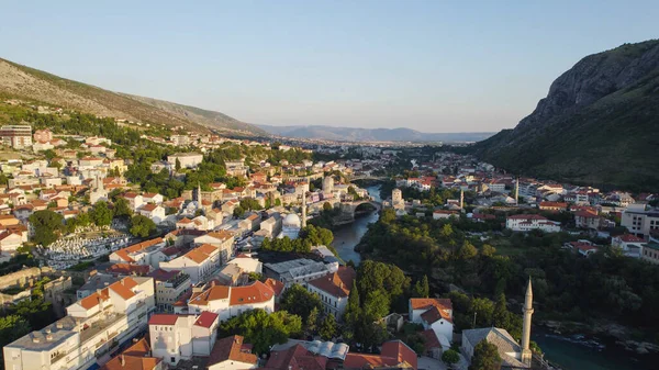 Mostar 'ın güzel şehir manzarasını gösteren hava aracı fotoğrafı Neretva Nehri ve Stari Most ikonik köprüsü, tarihi mimari ve manzaralı Balkan tepeleriyle çevrili..