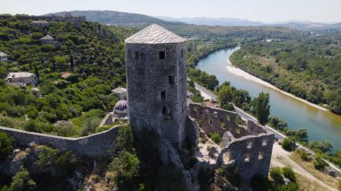 Bosna-Hersek 'teki yeşil tepeler ve taş evlerle çevrili Neretva Nehri' ne bakan ortaçağ Pocitelj Kalesi 'ni gösteren insansız hava aracı fotoğrafı.