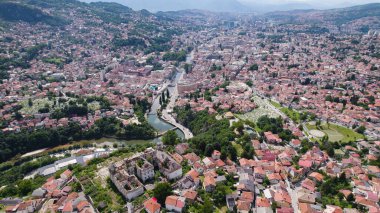 Saraybosna 'nın nehir kenarındaki köprüleri, tarihi ve modern binaları ve Bosna-Hersek' teki çevre tepeleri gösteren insansız hava aracı fotoğrafı.