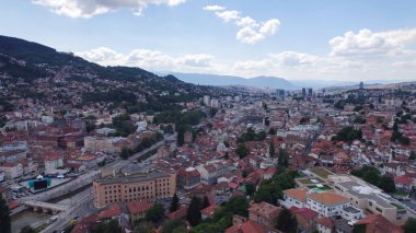 Saraybosna Belediye Binası 'nın Saraybosna' da kent binaları, köprüler ve şehir sokaklarıyla çevrili olduğunu gösteren hava aracı fotoğrafı.
