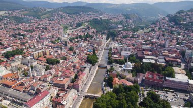 Nehir boyunca Saraybosna 'nın köprüleri, tarihi ve modern binaları ve çevresindeki tepeleri gösteren insansız hava aracı fotoğrafı.