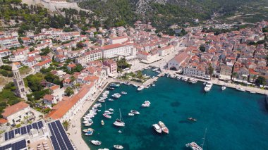 Hvar limanının Adriyatik Denizi kıyı şeridi boyunca renkli taş evler ve teknelerle dolu olduğu gösteren insansız hava aracı fotoğrafı..