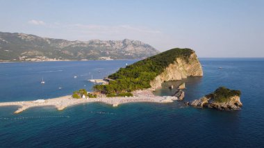 İnsansız hava aracı fotoğrafı, Karadağ 'ın Budva kentindeki Sveti Nikola Adası' nın temiz turkuaz sularla çevrili tam manzarasını gösteriyor. Doğal güzelliği ve sahil cazibesiyle Adriyatik adası manzarası.