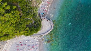İnsansız hava aracı fotoğrafı, Karadağ 'ın Budva kentindeki Sveti Nikola Adası yakınlarındaki berrak mavi sulara bakan yemyeşil bir kayalık gösteriyor. Doğal dokuları ve Akdeniz güzelliği ile canlı bir Adriyatik sahnesi.