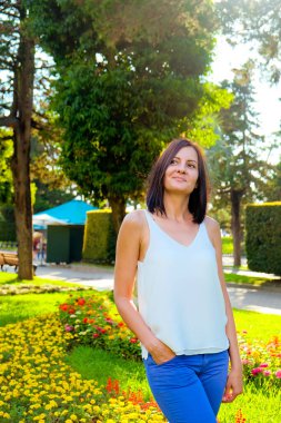 Renkli çiçeklerle poz veren romantik bir kadın. Neşeli, gülümseyen, açık havada beyaz bluzlu şanslı kadın. Güneşli yaz günü.