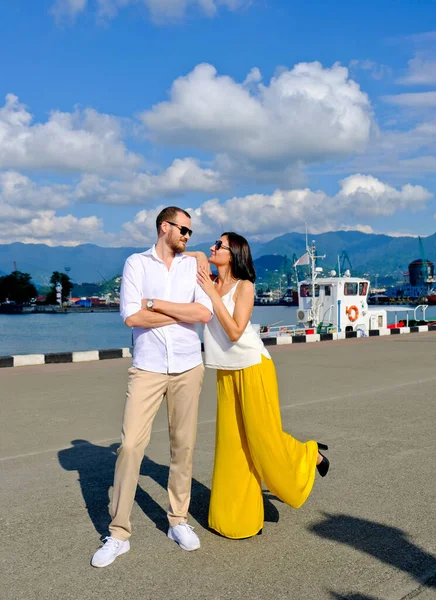 一对快乐的恋人在港口散步 山脉为背景 身穿白衬衫和黄色长裤 身穿白衣和幸运女子的快乐 微笑的男人 在海港的室外 — 图库照片