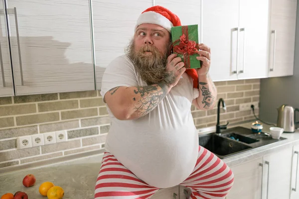 Emotional fat funny and tattooed man with present at the kitchen at home