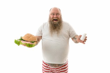 Duygusal açıdan şişman, komik ve dövmeli bir adam. Beyaz bir arka planda izole edilmiş yiyecekleri var.