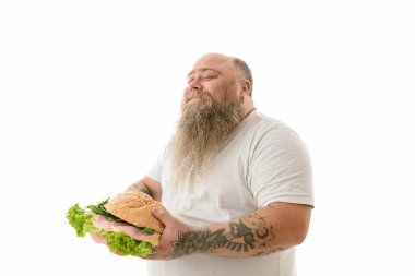 Duygusal açıdan şişman, komik ve dövmeli bir adam. Beyaz bir arka planda izole edilmiş yiyecekleri var.