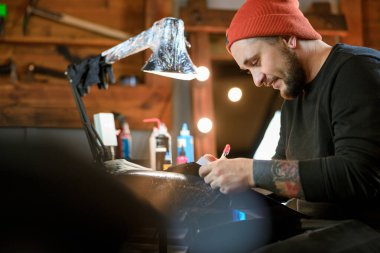 Profesyonel Sakallı Kafkas dövme ustası rahat atmosferik stüdyoda çalışıyor.