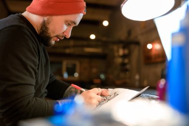 Profesyonel Sakallı Kafkas dövme ustası rahat atmosferik stüdyoda çalışıyor.