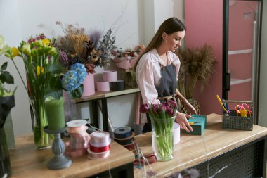 Profesyonel çiçekçi genç bayan çiçekçide buket yapıyor.