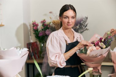 Profesyonel çiçekçi genç bayan çiçekçide buket yapıyor.