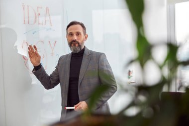 Ofisteki beyaz yetişkin adam cam masaya yazı yazıyor.