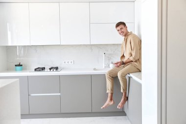 Mutlu yakışıklı adam minimalist mutfakta duruyor ve gülümsüyor.