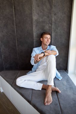 Mutlu yetişkin beyaz erkek panoramik pencerenin yanında oturuyor ve ürperiyor.