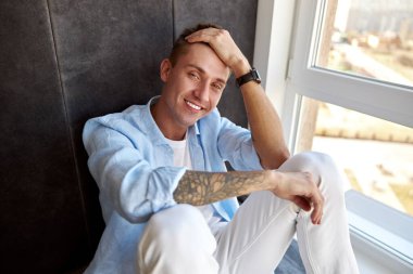 Mutlu yetişkin beyaz erkek panoramik pencerenin yanında oturuyor ve ürperiyor.