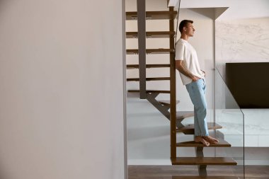Modern ışıklı apartmanın minimalist merdivenlerinde rahatlayan mutlu beyaz adam.