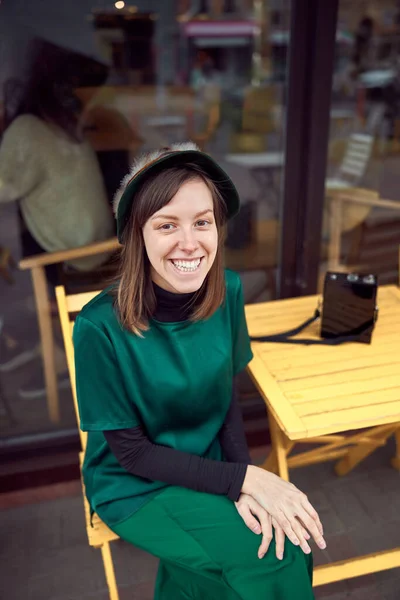 Ritratto di allegra giovane donna caucasica in abiti verdi che seduta fuori dal caffè — Foto Stock