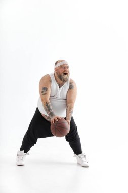 Beyaz arka planda basketbol topu olan sakallı, beyaz, beyaz, beyaz, dövmeli bir adam. Komik ve mutlu.