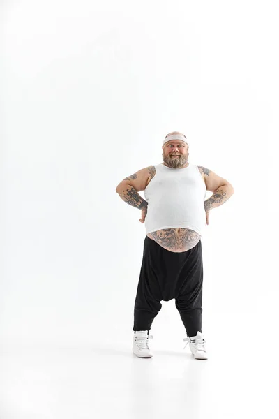 Happy dikke man met grote buik en tattoes in sportkleding poseren op witte achtergrond — Stockfoto