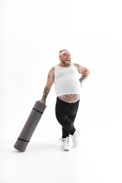 Vrolijke dikke man met dikke buik en tattos in sportkleding met trainingsmat — Stockfoto