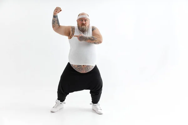 Homem gordo feliz com barriga grande e tatuagens em roupas esportivas posando no fundo branco — Fotografia de Stock