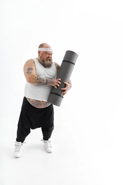 Щасливий товстий чоловік з великим животом і батогами в спортивному одязі з тренувальним килимком — стокове фото