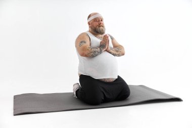 Sakallı ve dövmeli şişman adam yoga yapıyor.