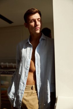 Mutlu, güzel, yakışıklı, gülümseyen beyaz adam sabah güneşinde modern ışık evinde dinleniyor.