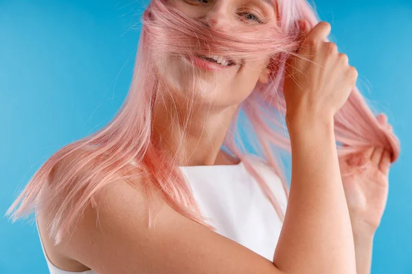 Porträt der schönen weiblichen Modell spielt mit rosa Haaren, wickelt es um ihr Gesicht, während posiert isoliert über blauem Studiohintergrund — Stockfoto