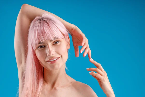 ピンク色の髪と完璧な肌の笑顔を持つ裸の入れ墨の女性の肖像カメラで,青のスタジオの背景に隔離された手でポーズ — ストック写真