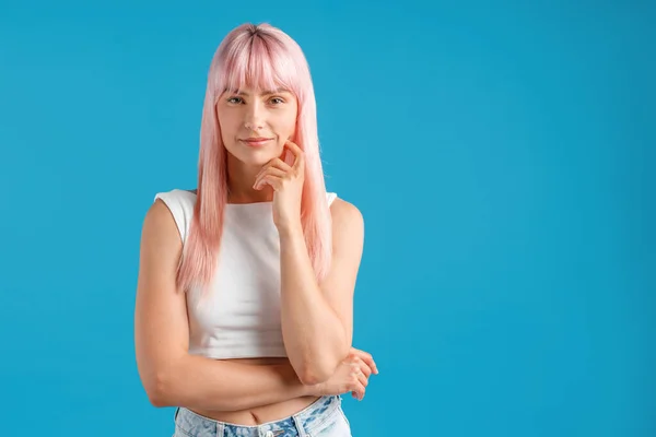 Schöne junge Frau mit rosa Haaren blickt in die Kamera, steht isoliert über blauem Studiohintergrund — Stockfoto