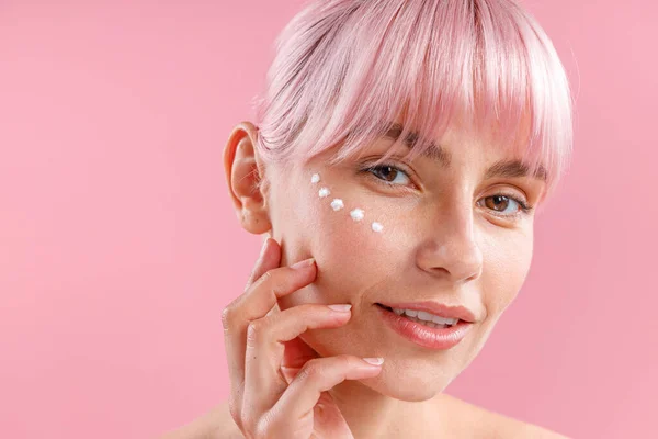 Porträt einer charmanten Frau mit rosa Haaren und Gesichtscreme auf der Haut wie Punkte auf rosa Hintergrund isoliert — Stockfoto
