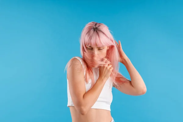 Atractiva modelo femenina en camisa blanca mirando hacia abajo, ocultando su cara con pelo rosa mientras posa aislada sobre fondo azul del estudio — Foto de Stock