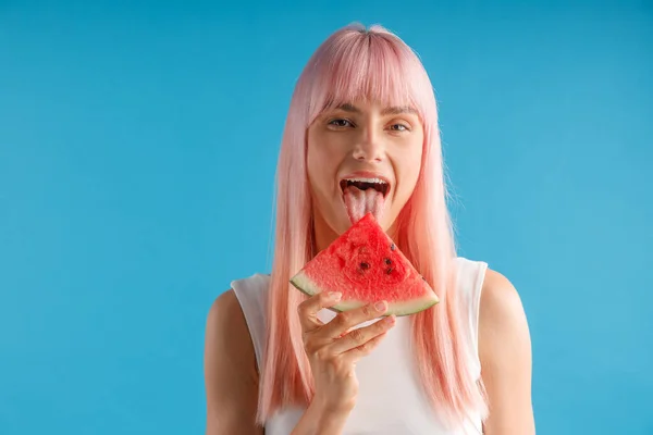 Verspielte junge Frau mit rosa Haaren, die eine Scheibe Wassermelone hält, posiert mit offenem Mund isoliert vor blauem Studiohintergrund — Stockfoto