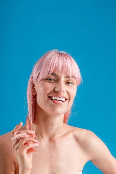 Retrato de una hermosa mujer desnuda sonriendo a la cámara, tocando su cabello liso rosa mientras posa aislada sobre el fondo azul del estudio — Foto de Stock
